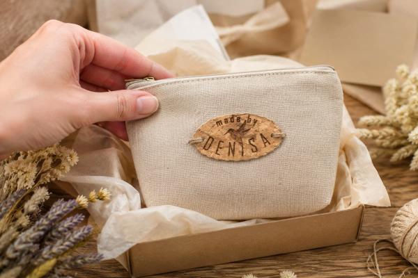 Étiquette ovale en liège « made by Denisa » cousue sur une pochette en tissu beige.